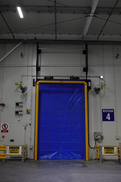 Blue high-speed insulated fabric door with yellow frame in a warehouse.