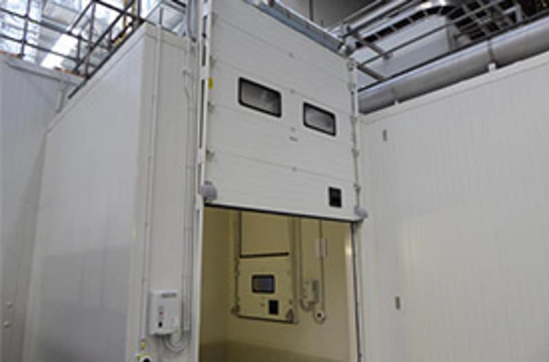 White insulated sectional overhead door partially open in a facility.