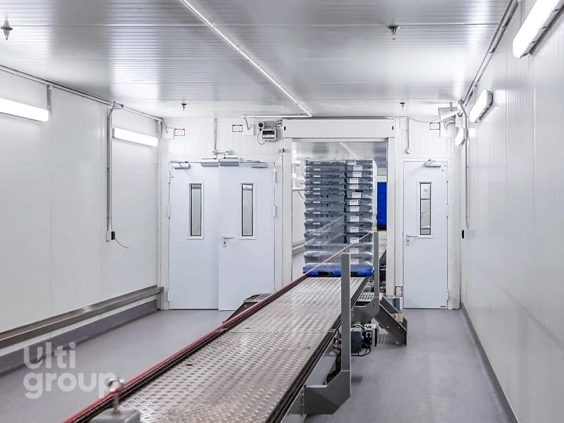 Conveyor system transporting a stack of crates through an automated doorway.