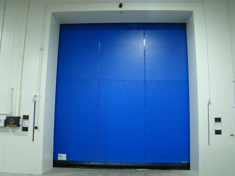 A large blue Ulti-Roll Insulated high speed door installed in a white warehouse wall.