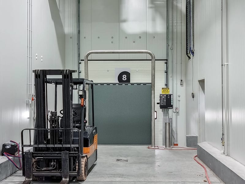 Forklift parked in front of a grey Ulti Fold Door at a loading dock.