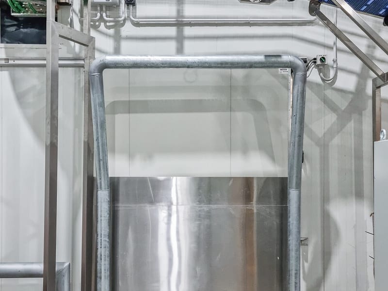 Galvanised steel goalpost bollard protecting a wall opening under a conveyor.