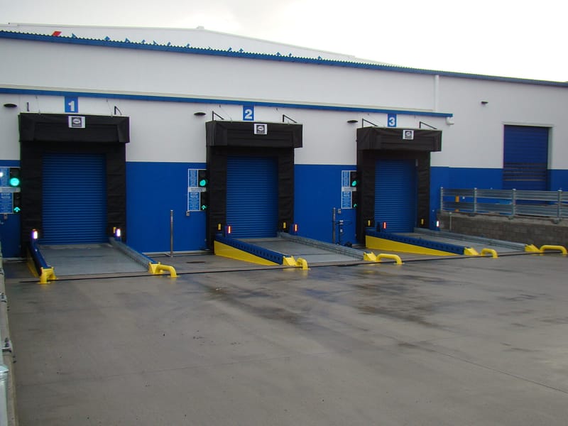 Three industrial loading docks with blue roller doors and yellow dock levellers.
