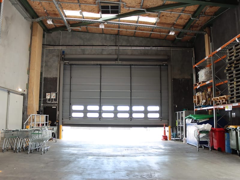 A large grey sectional overhead door partially open in a warehouse.