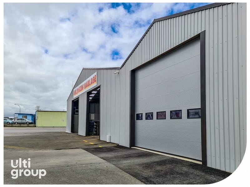 Grey sectional overhead door with vision panels on a corrugated metal warehouse.