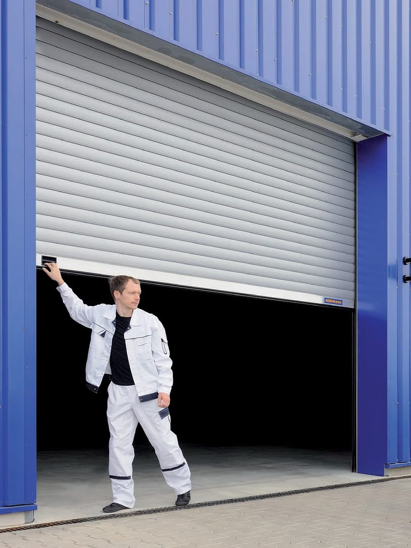 Technician in white workwear opening a grey industrial roller shutter door.