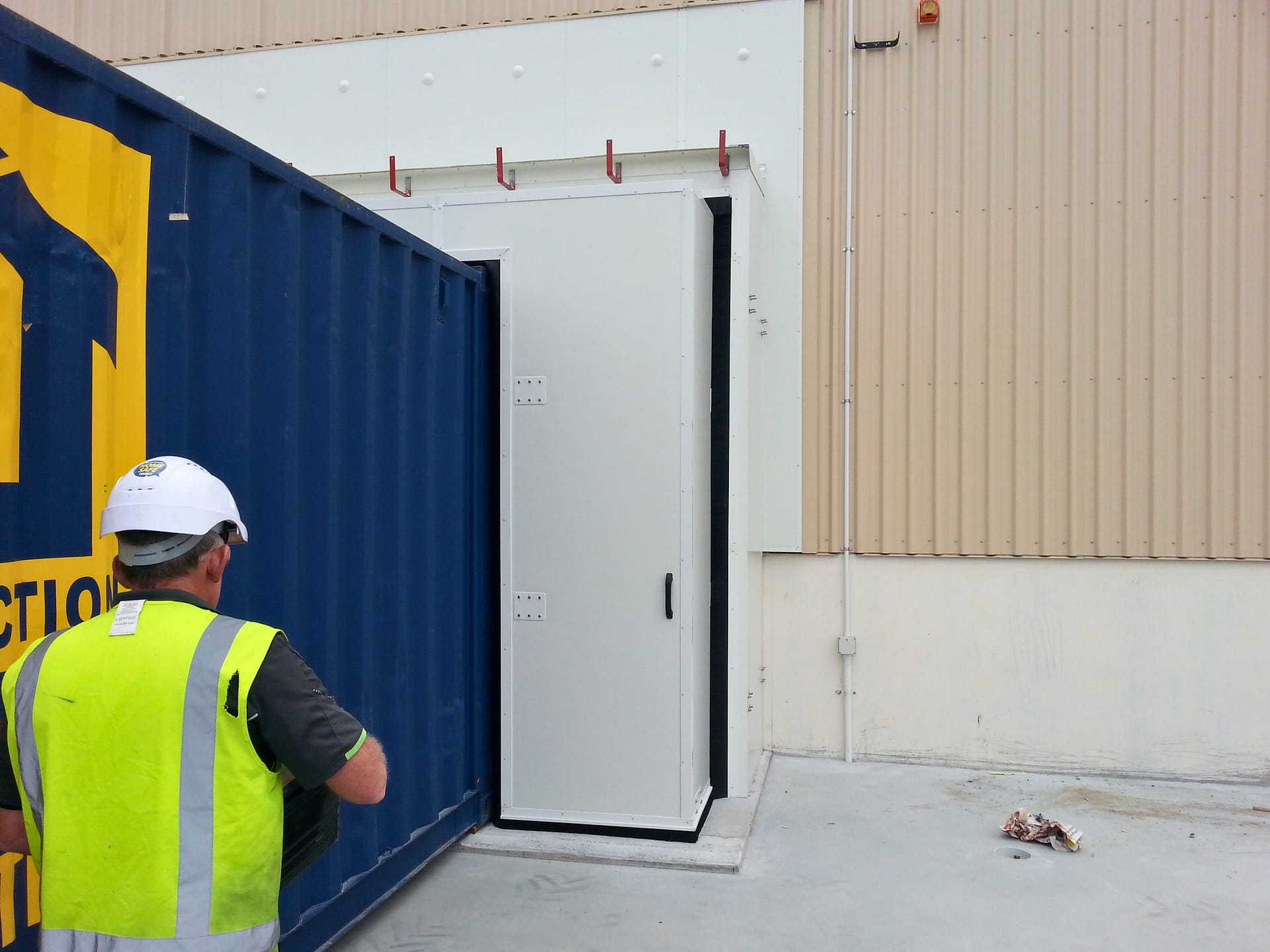 A worker in a high-visibility vest standing by a blue shipping container and white dock seal.
